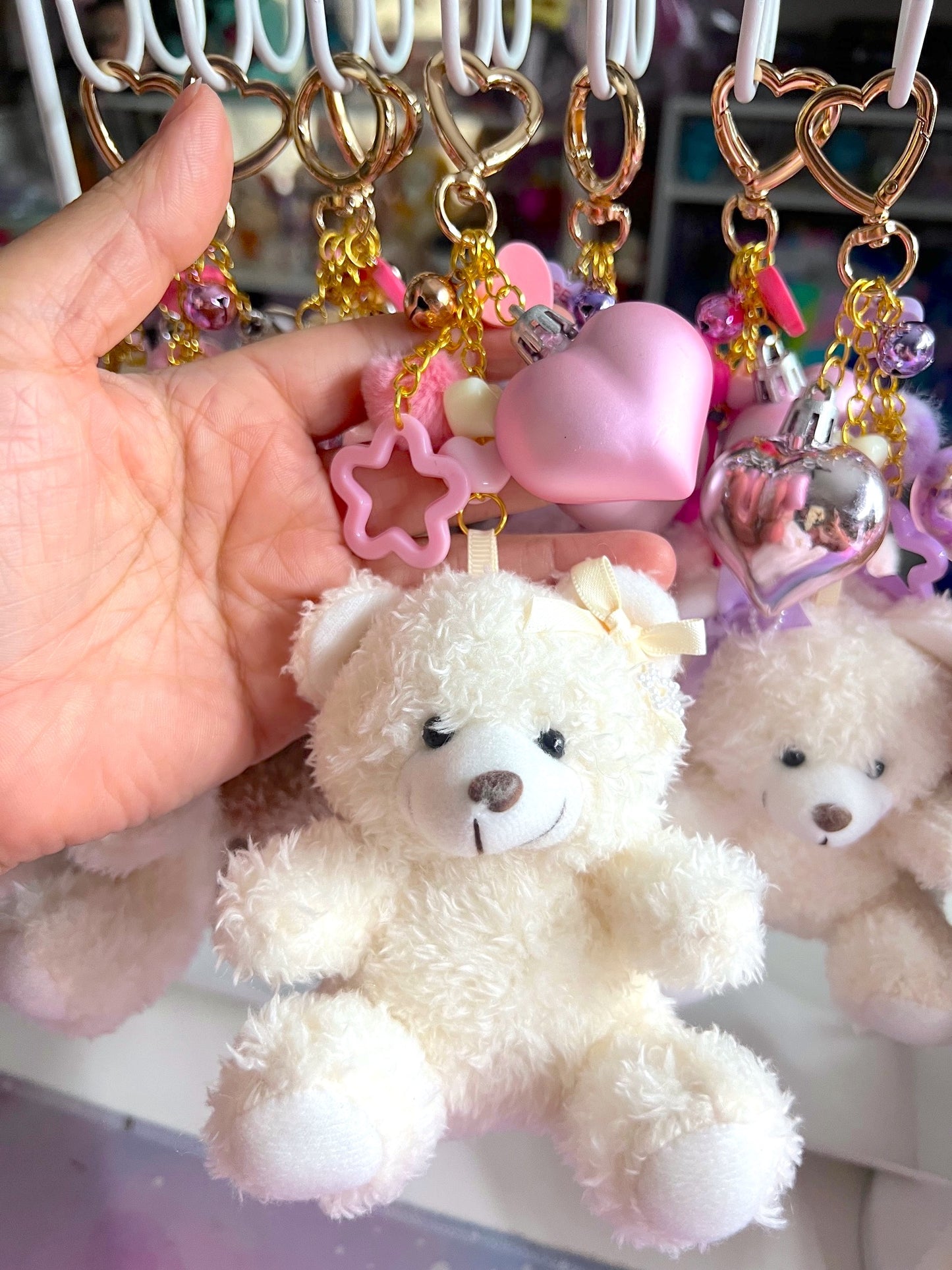Hand holding a teddy bear keychain with decorative elements on a blurred background