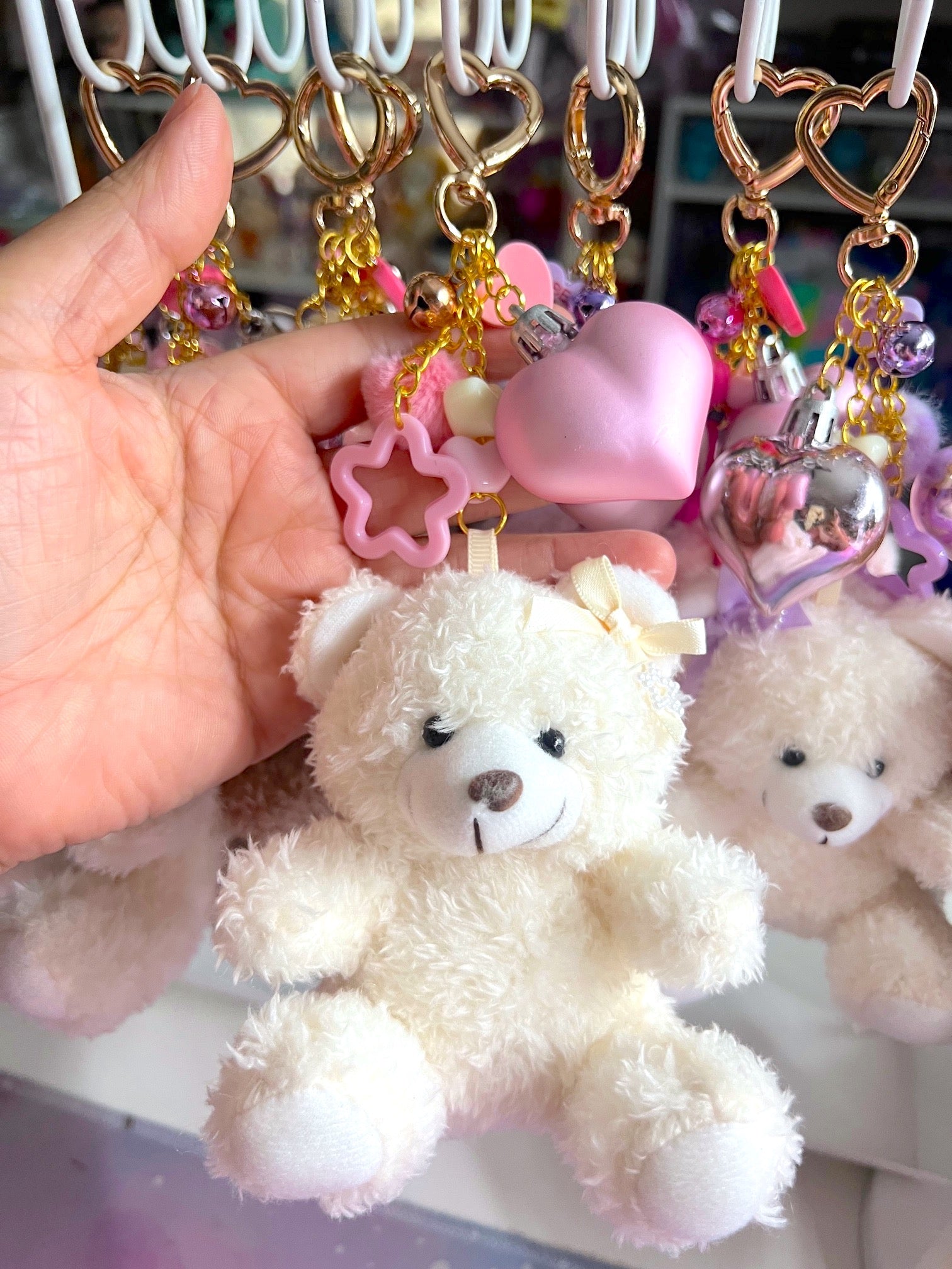Hand holding a teddy bear keychain with decorative elements on a blurred background