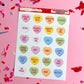 Sheet of colorful conversation heart stickers with text on a pink background with confetti.