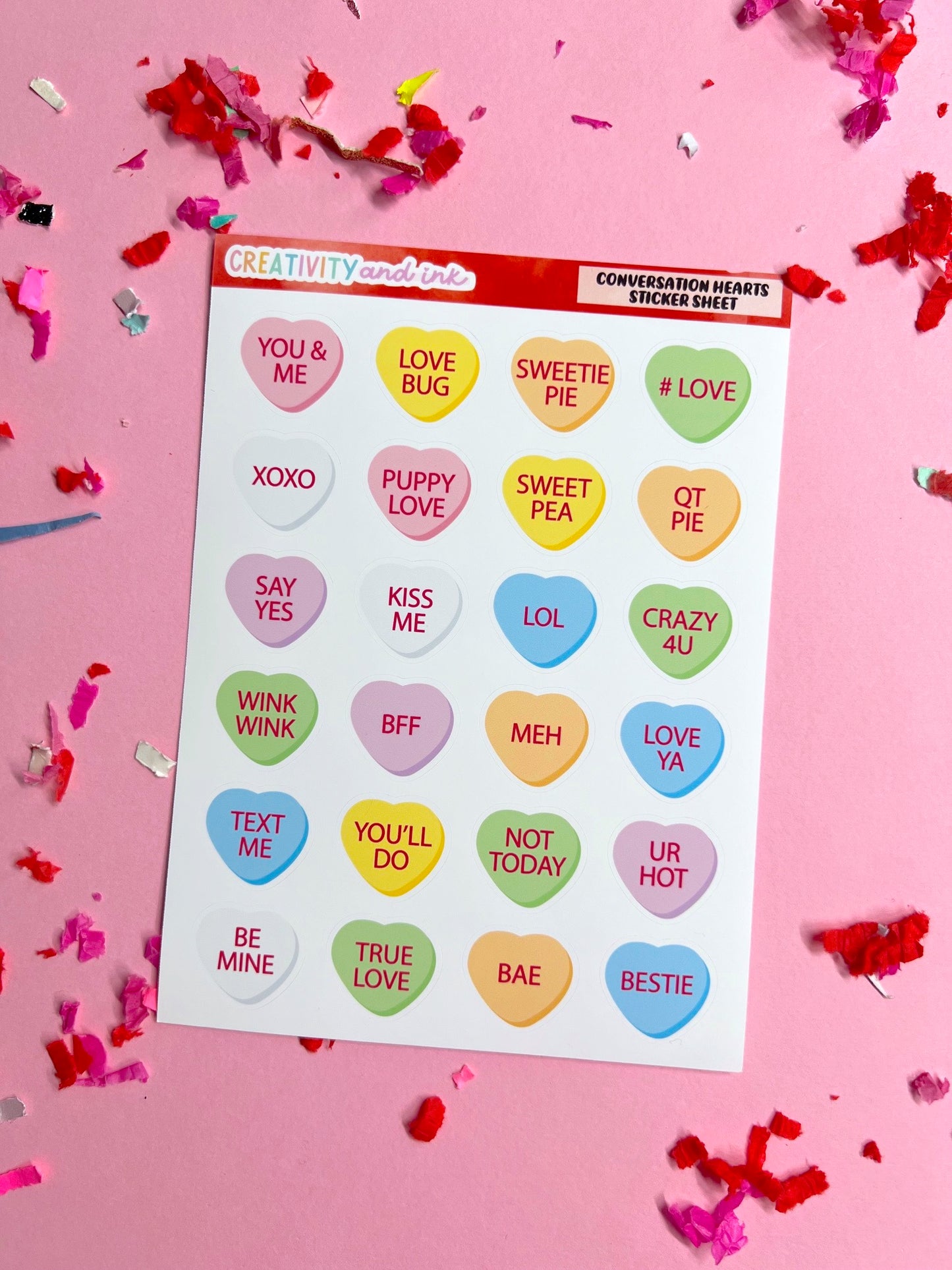 Sheet of colorful conversation heart stickers with text on a pink background with confetti.