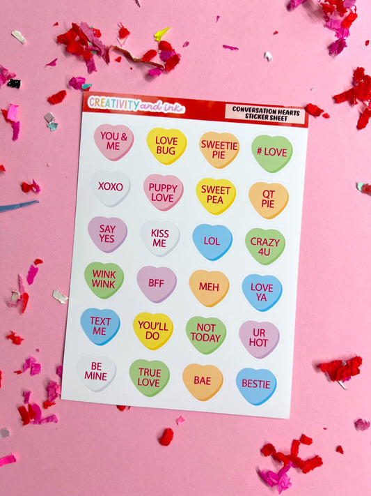 Sheet of colorful conversation heart stickers with text on a pink background with confetti.