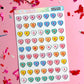 Sheet of colorful heart-shaped alphabet stickers on a pink background with confetti.