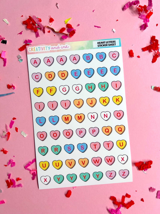 Sheet of colorful heart-shaped alphabet stickers on a pink background with confetti.
