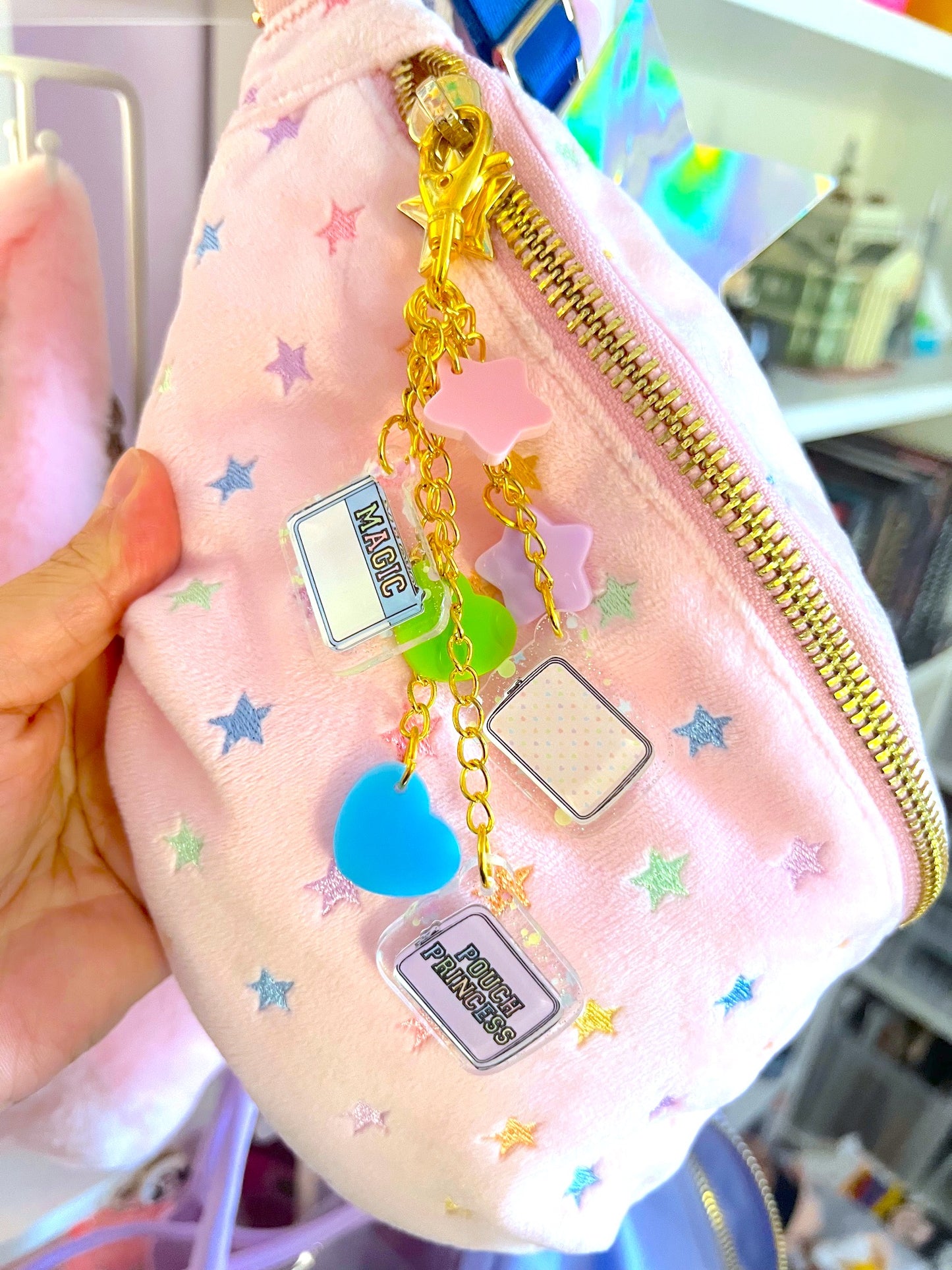 Pink pouch with gold zipper and decorative charms held by a hand.