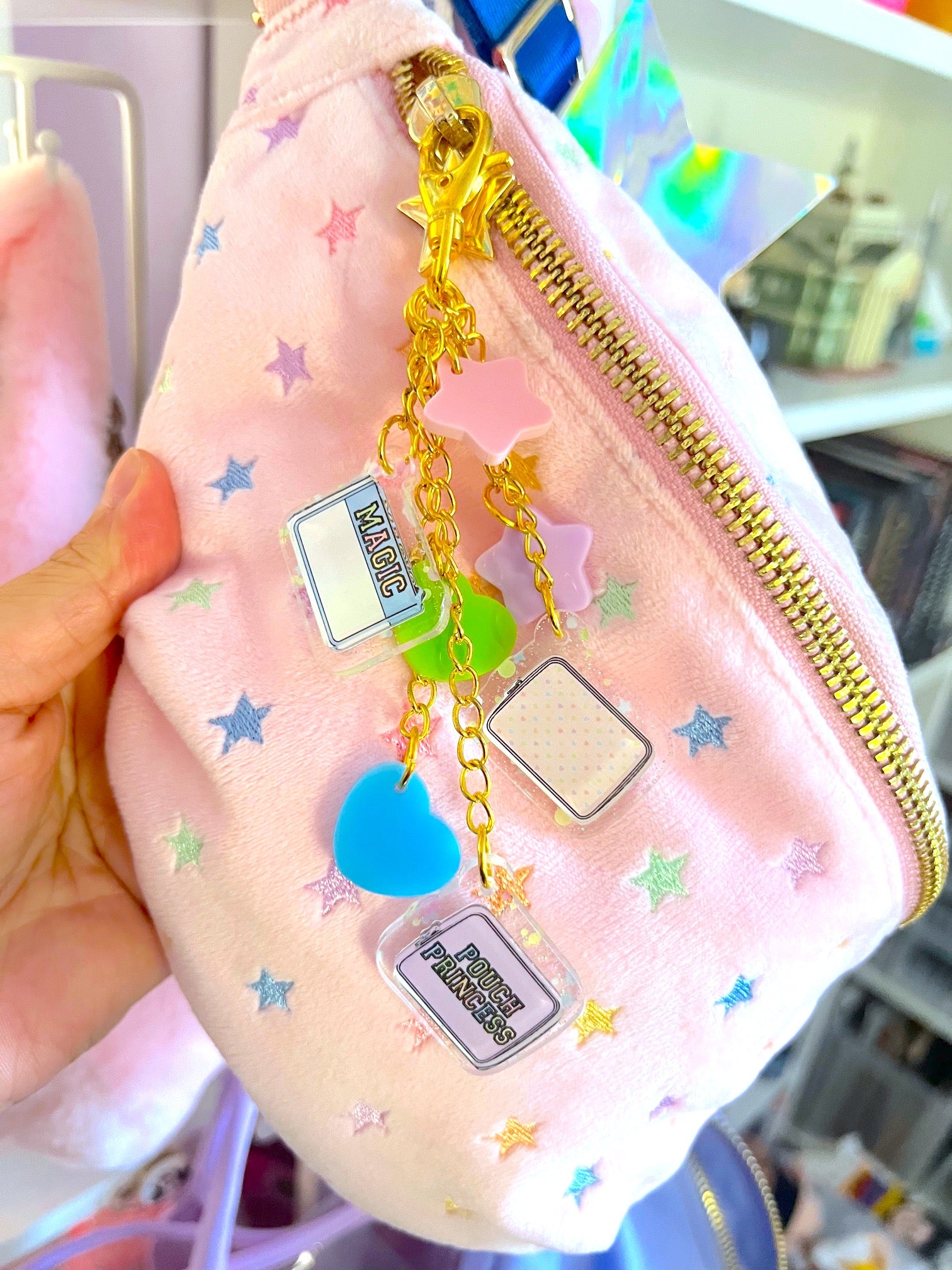 Pink pouch with gold zipper and decorative charms held by a hand.