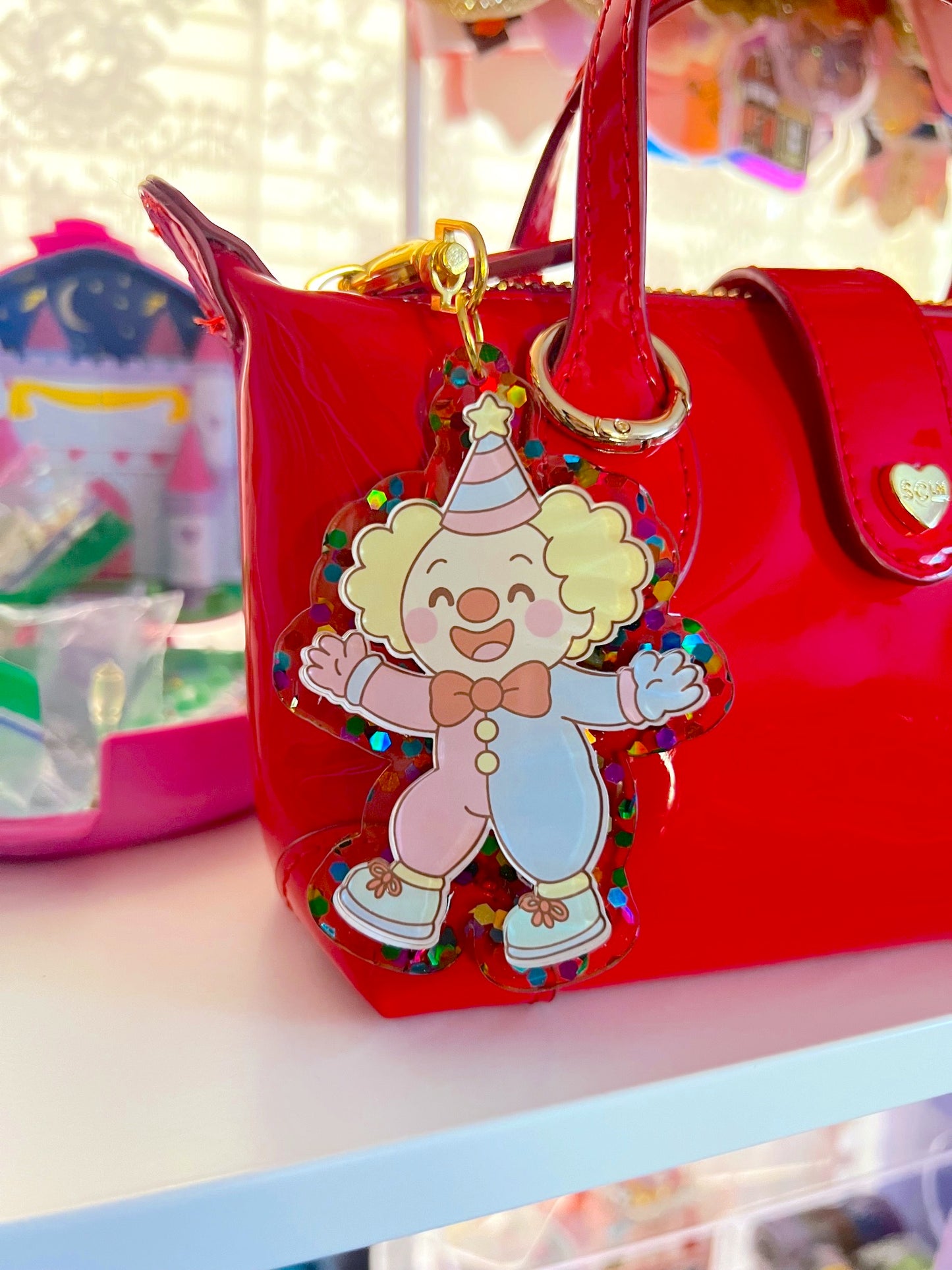 Red handbag with a colorful clown charm on a shelf.