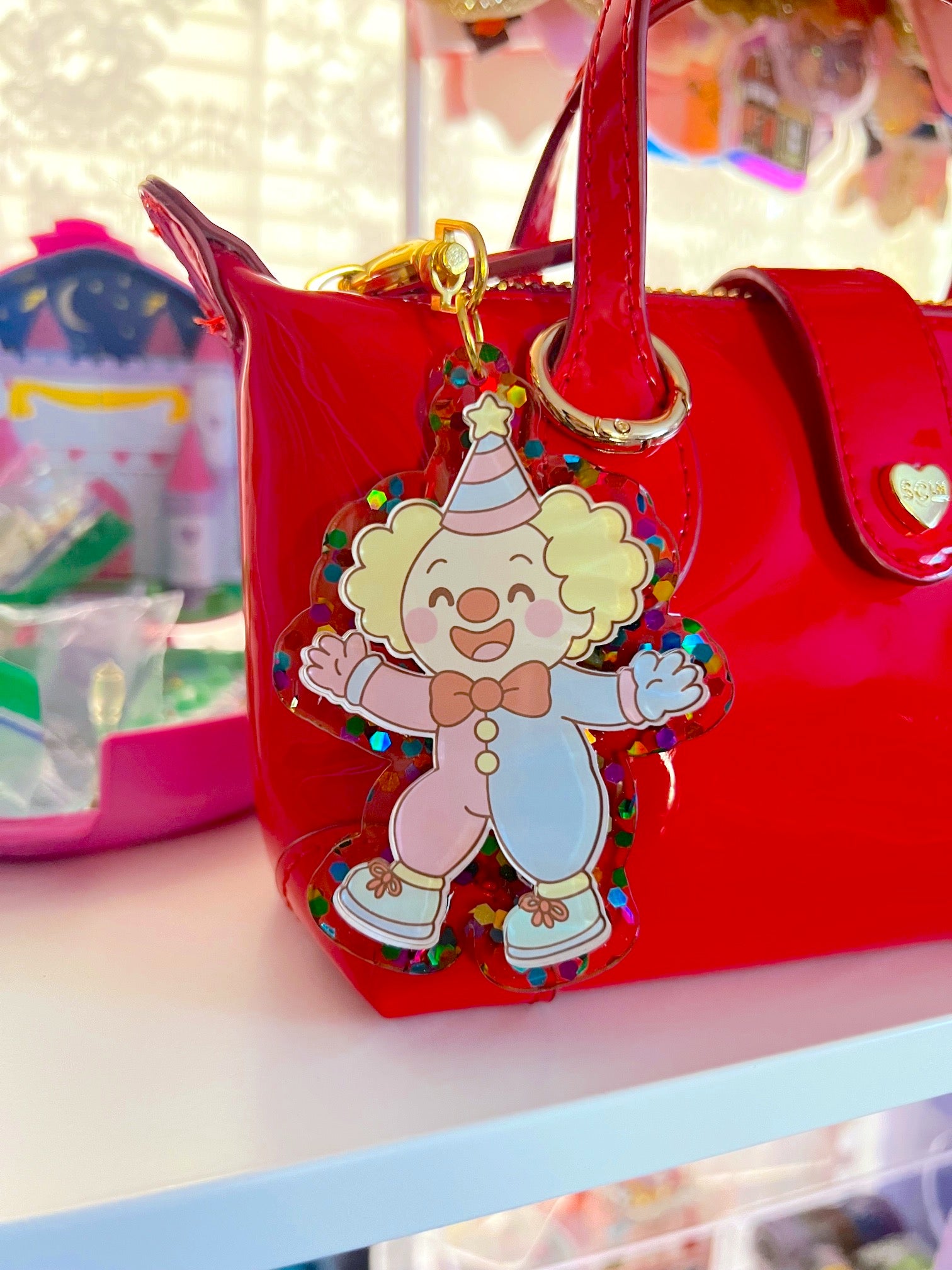 Red handbag with a colorful clown charm on a shelf.