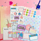 Colorful stationery items including stickers and a planner on a pink background