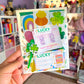 Hand holding a colorful mini scrapbook pack with 'Lucky' theme in a store setting.