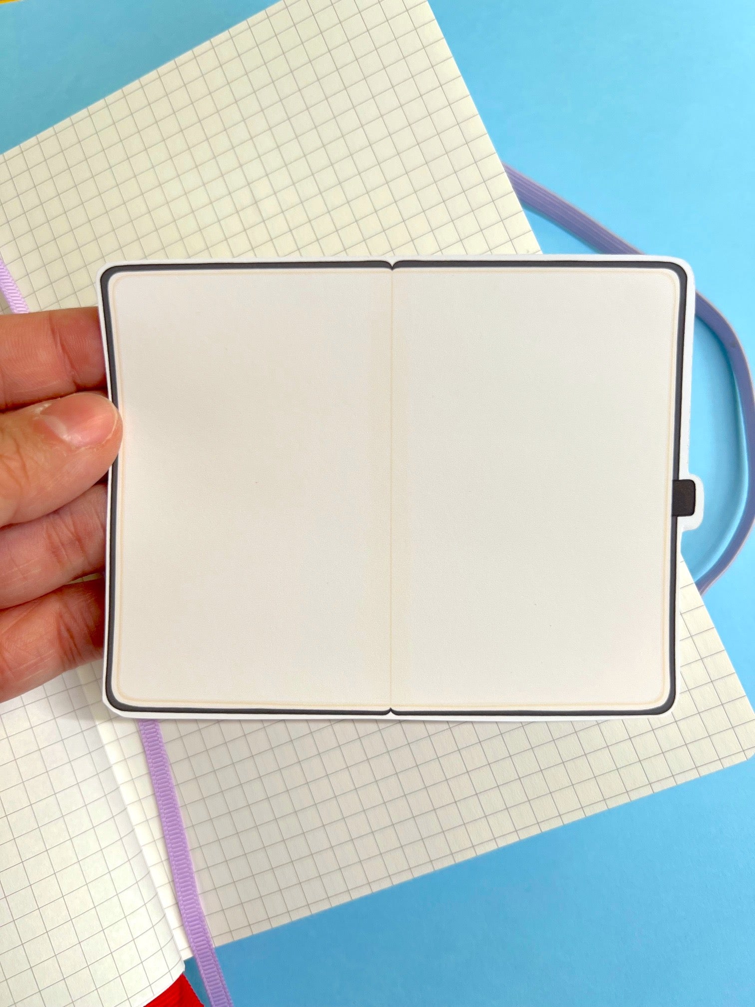 Hand holding a small notebook with grid paper on a blue background