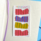Striped adhesive strips in red, blue, and green on a notebook page 