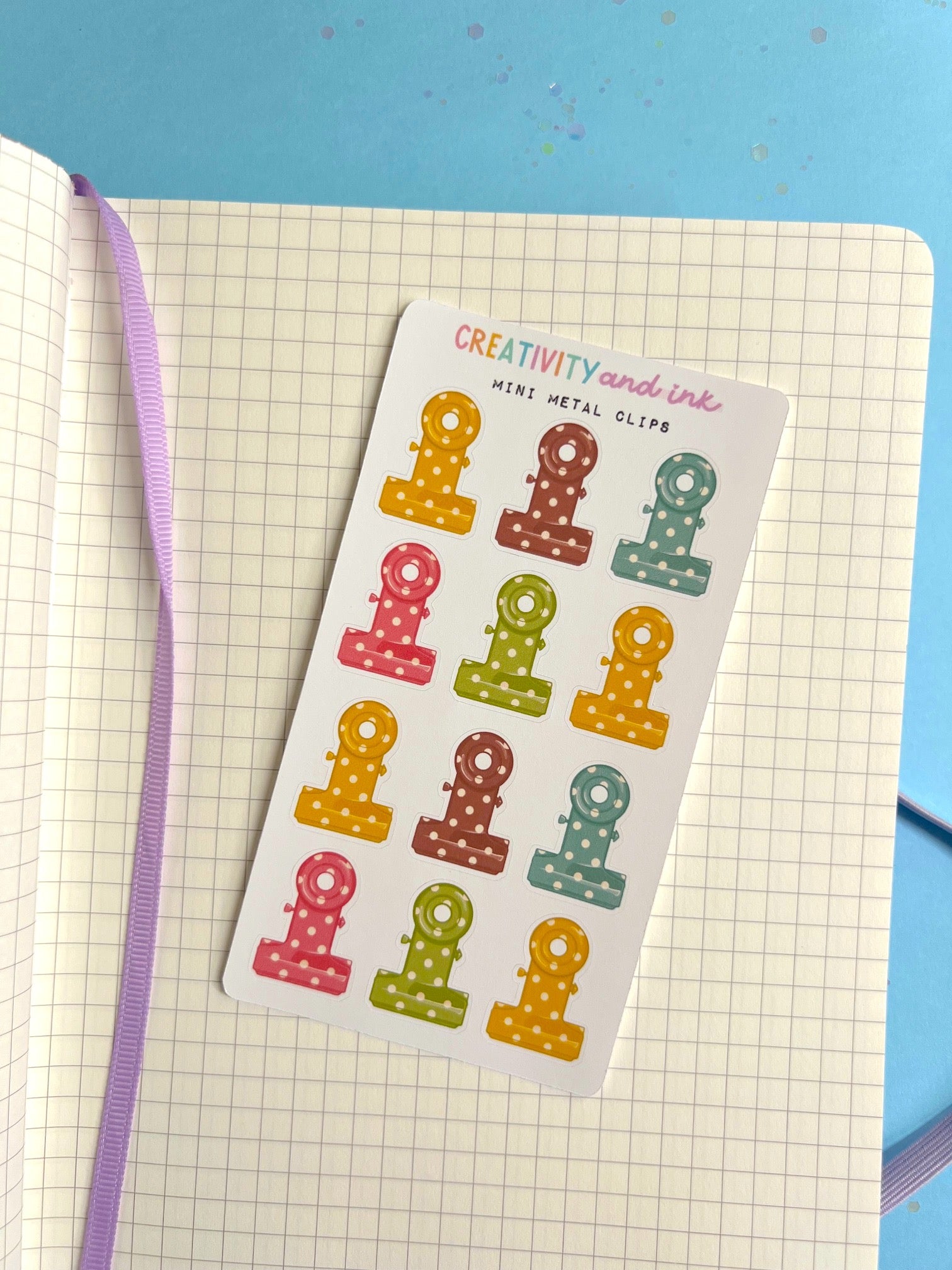Sheet of colorful mini metal clips on a notebook page with a blue background