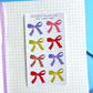 Pack of mini fabric bows with colorful designs on a notebook page.