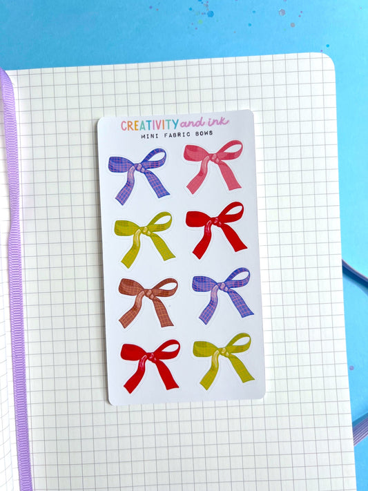 Pack of mini fabric bows with colorful designs on a notebook page.