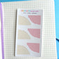 Pack of mini paper corners with grid and solid designs on a notebook page.