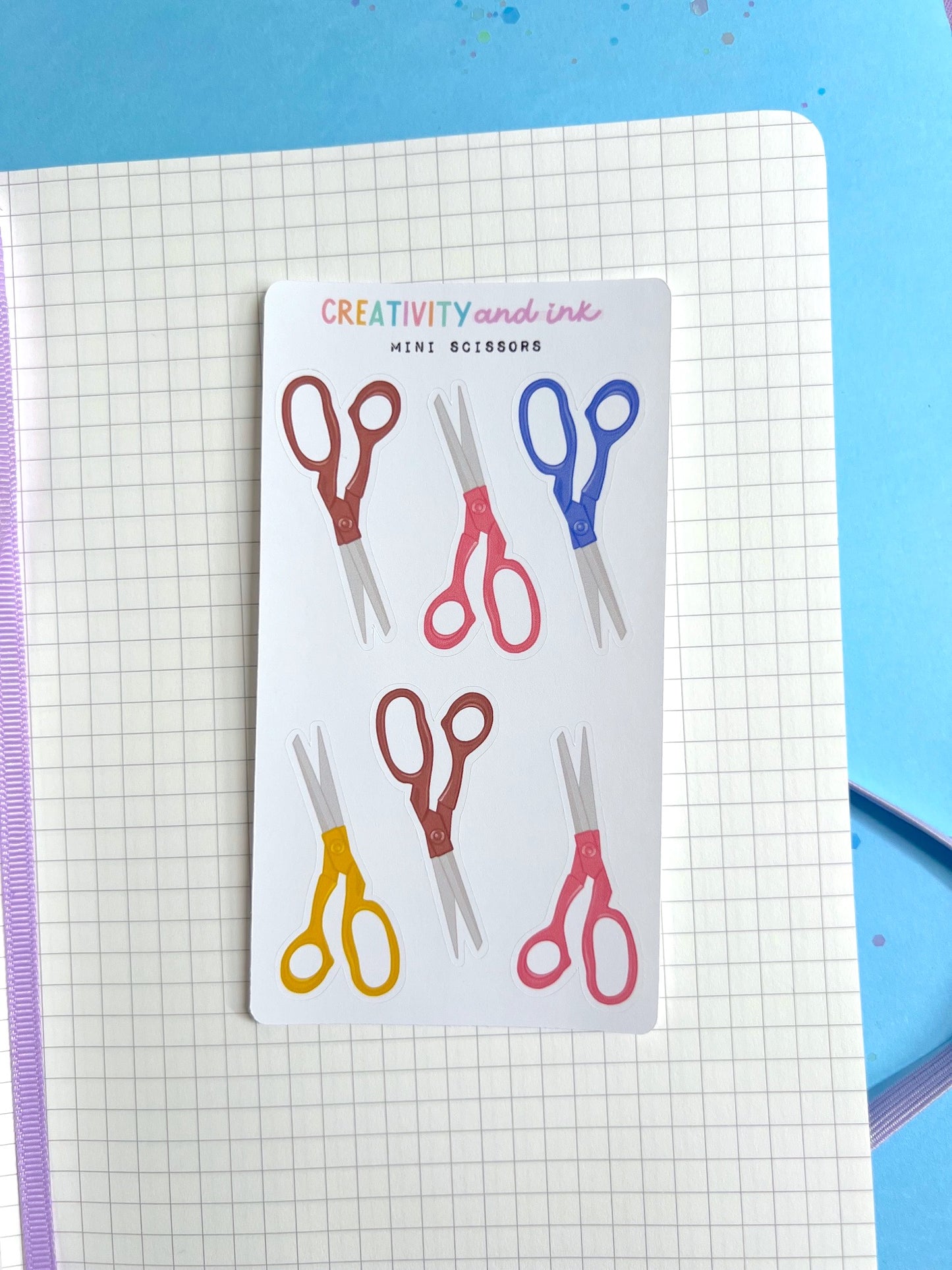 Sheet of colorful scissors stickers on a grid notebook page 